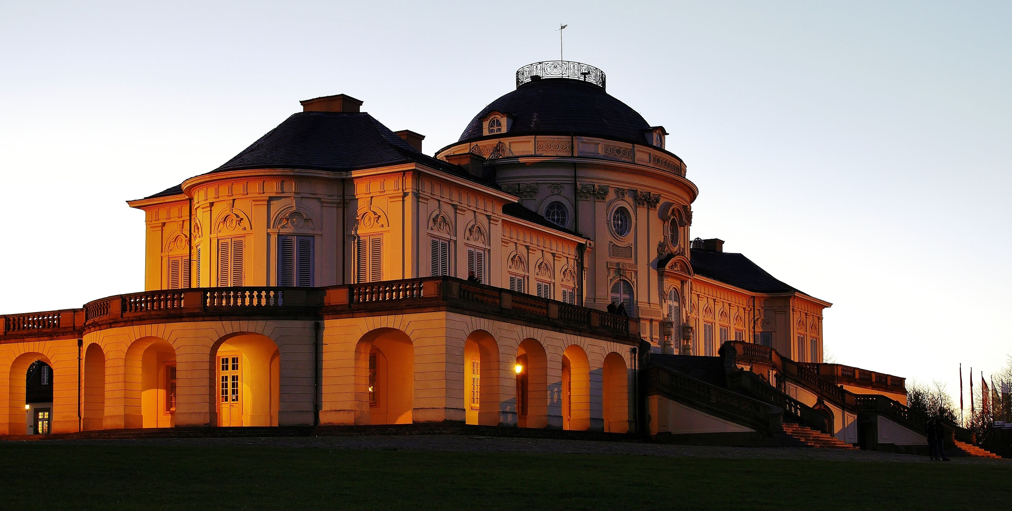 A large, ornate building with a dome and multiple arches at dusk.