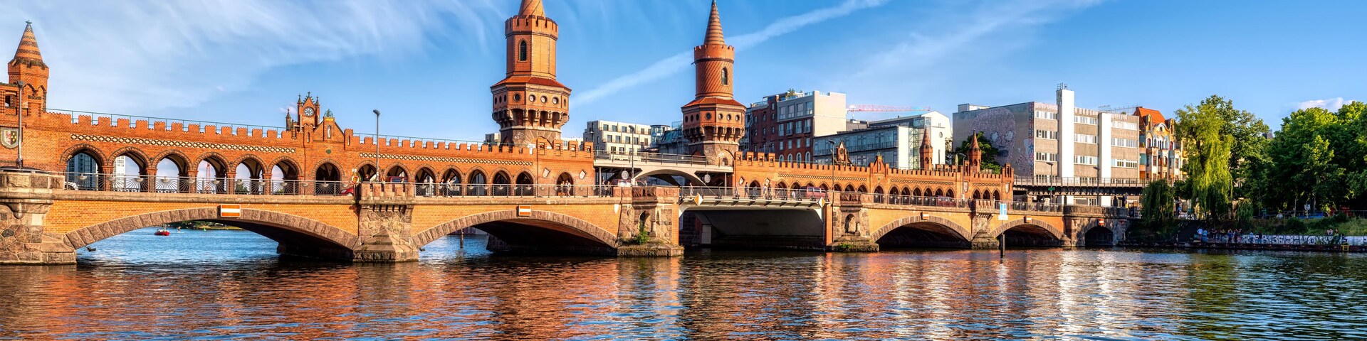 A historic bridge with two towers, a river, and modern buildings in the background.