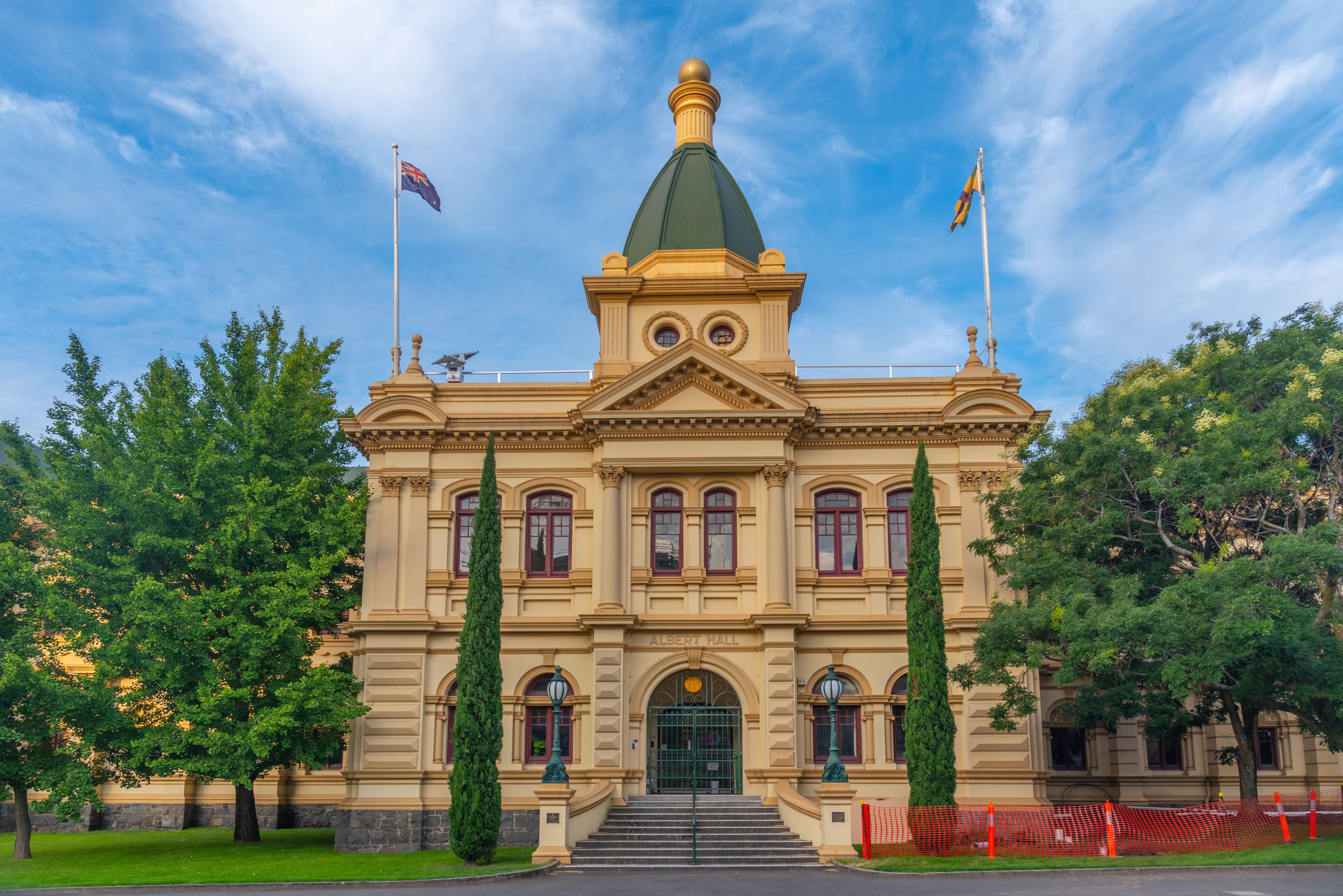 A neoclassical building with a green dome, two flags, and a central entrance.