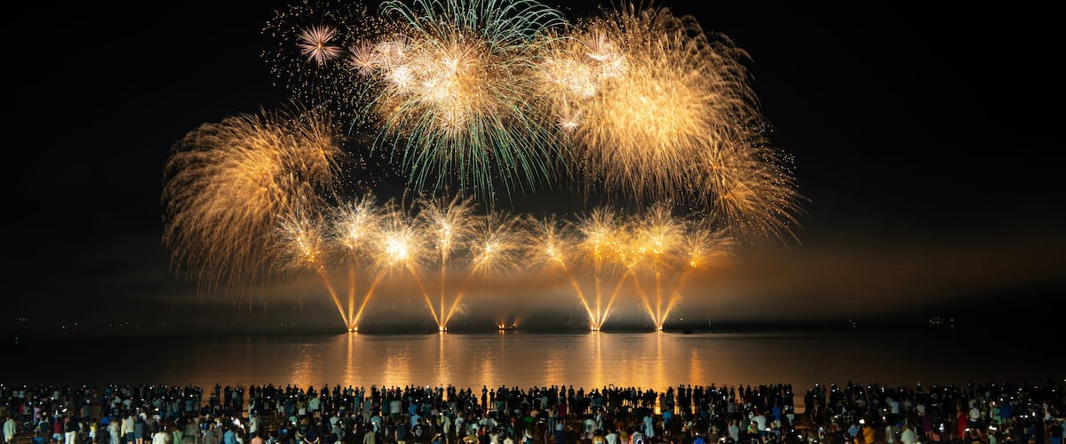 A nighttime fireworks display over a body of water with a crowd of people watching.