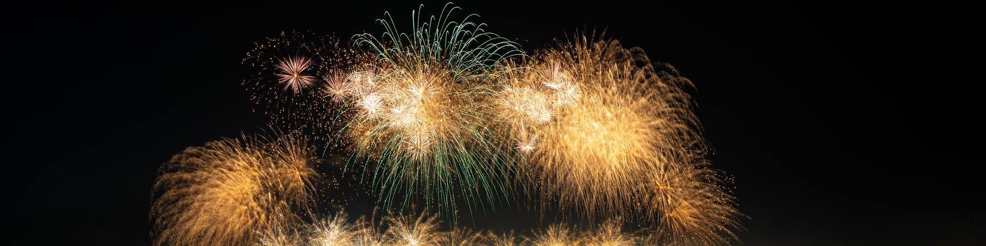A nighttime fireworks display over a body of water with a crowd of people watching.
