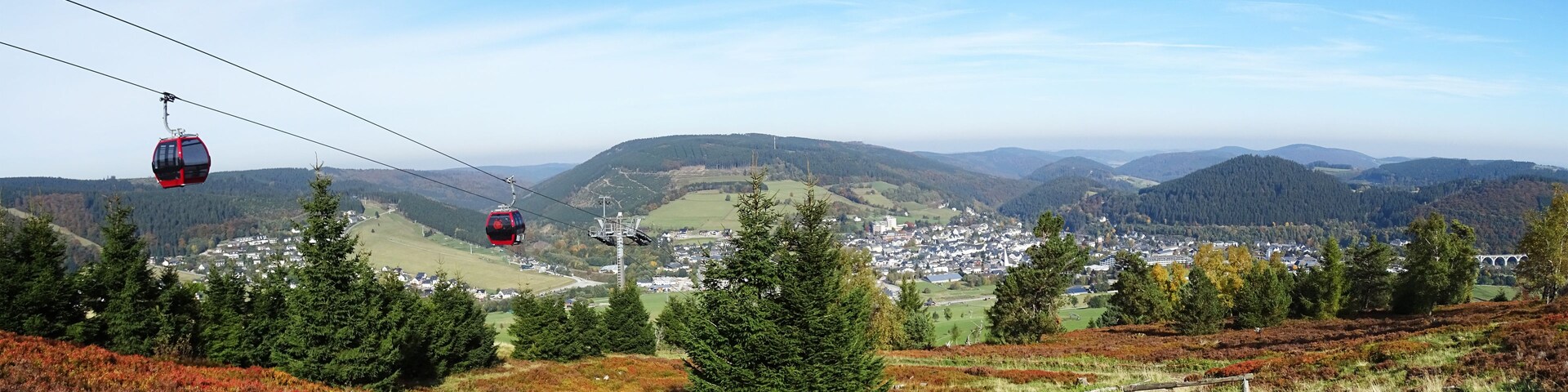 Eine Seilbahn, eine Stadt und eine gebirgige Landschaft.