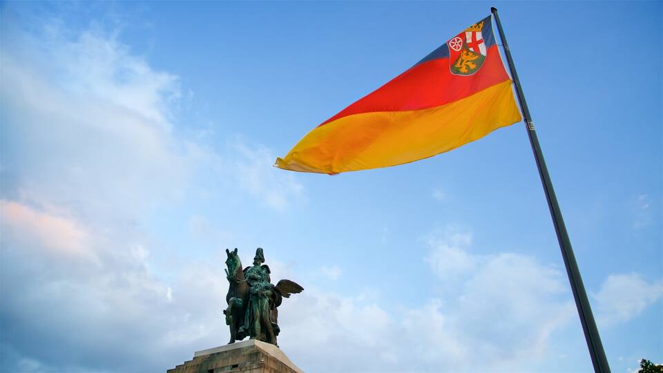 Una bandera con un escudo, una estatua y un cielo azul despejado.