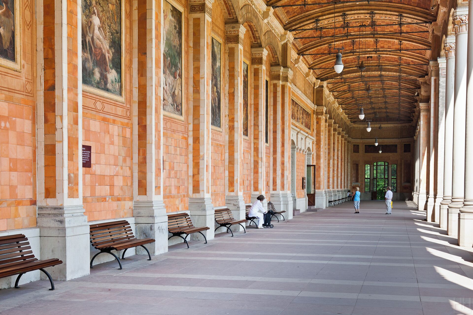 A covered walkway with benches, columns, and murals.
