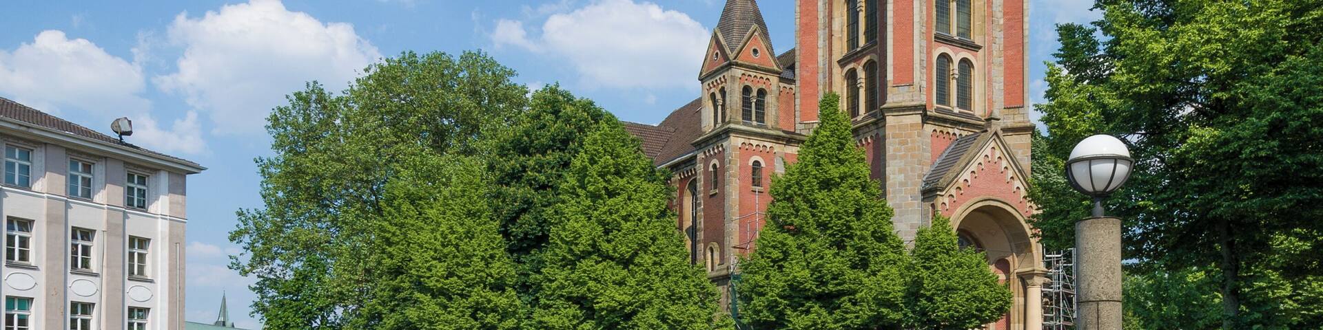 A historic church with a tall tower, surrounded by trees and a paved courtyard.