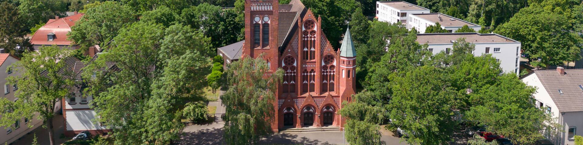 A church with a tall spire, surrounded by trees and residential buildings.