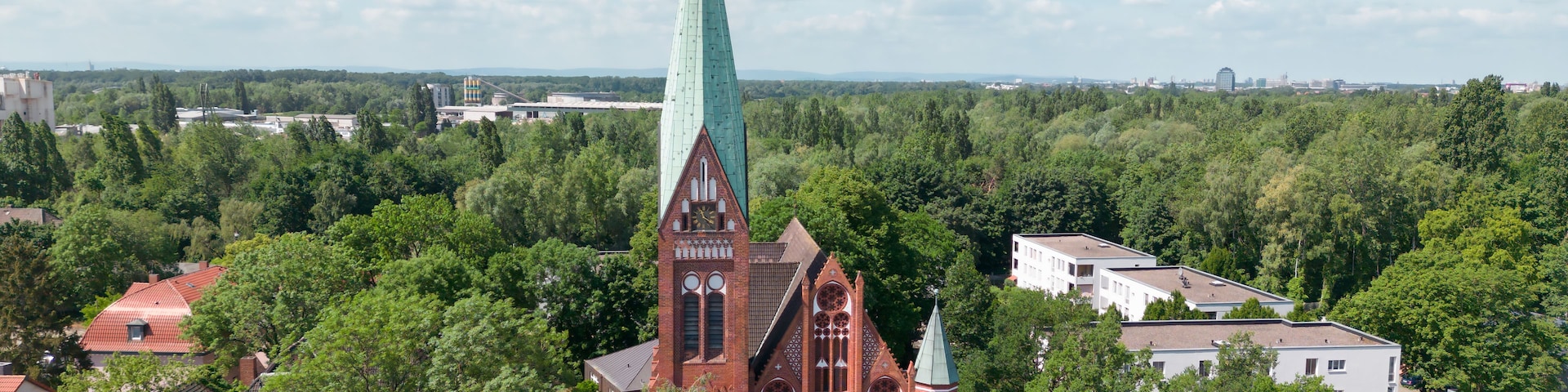 Igreja com uma torre alta, rodeada por árvores e edifícios residenciais.