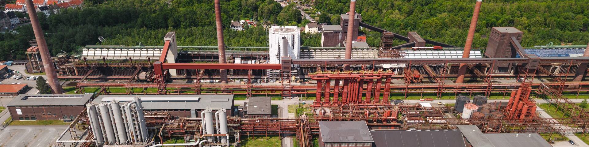 An industrial complex with multiple tall chimneys, storage tanks, and extensive piping.