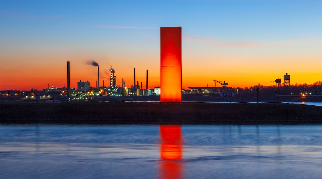 Tramonto su una zona industriale con una torre rossa ben visibile che si riflette nell'acqua.