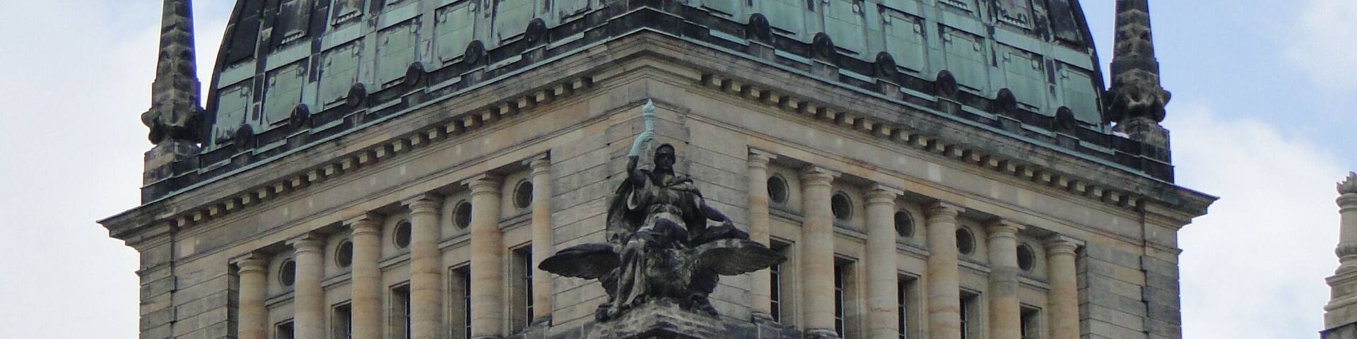 A large domed building with a statue on top and a smaller dome with a clock.