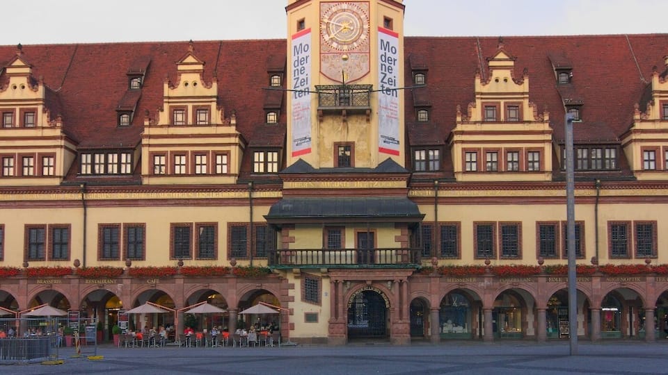 Un bâtiment historique doté d’une tour horlogée, de fenêtres en arc de cercle et d’une place pavée.