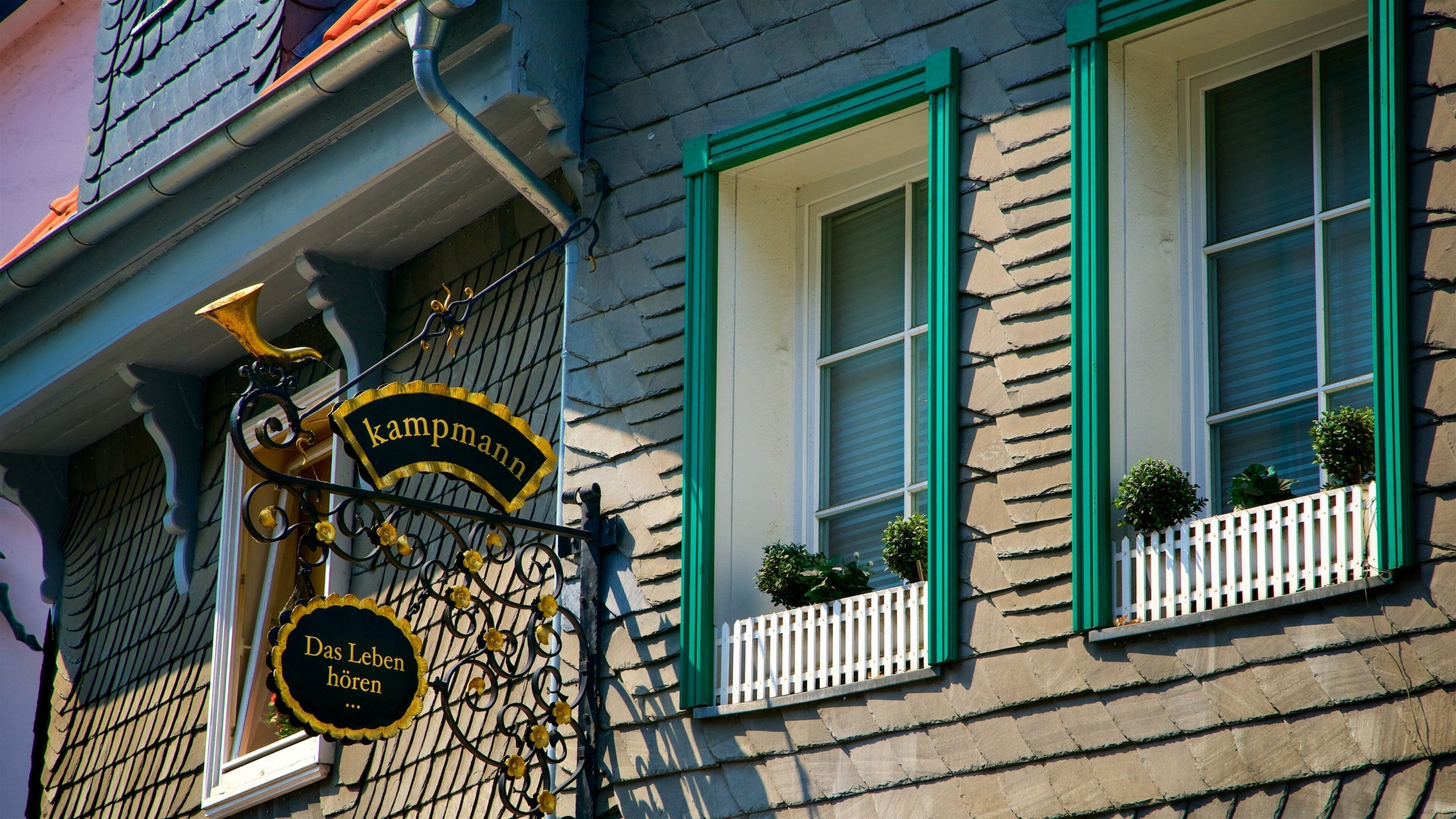 A building with green window frames, a sign reading "kampmann," and a sign saying "Das Leben hört."