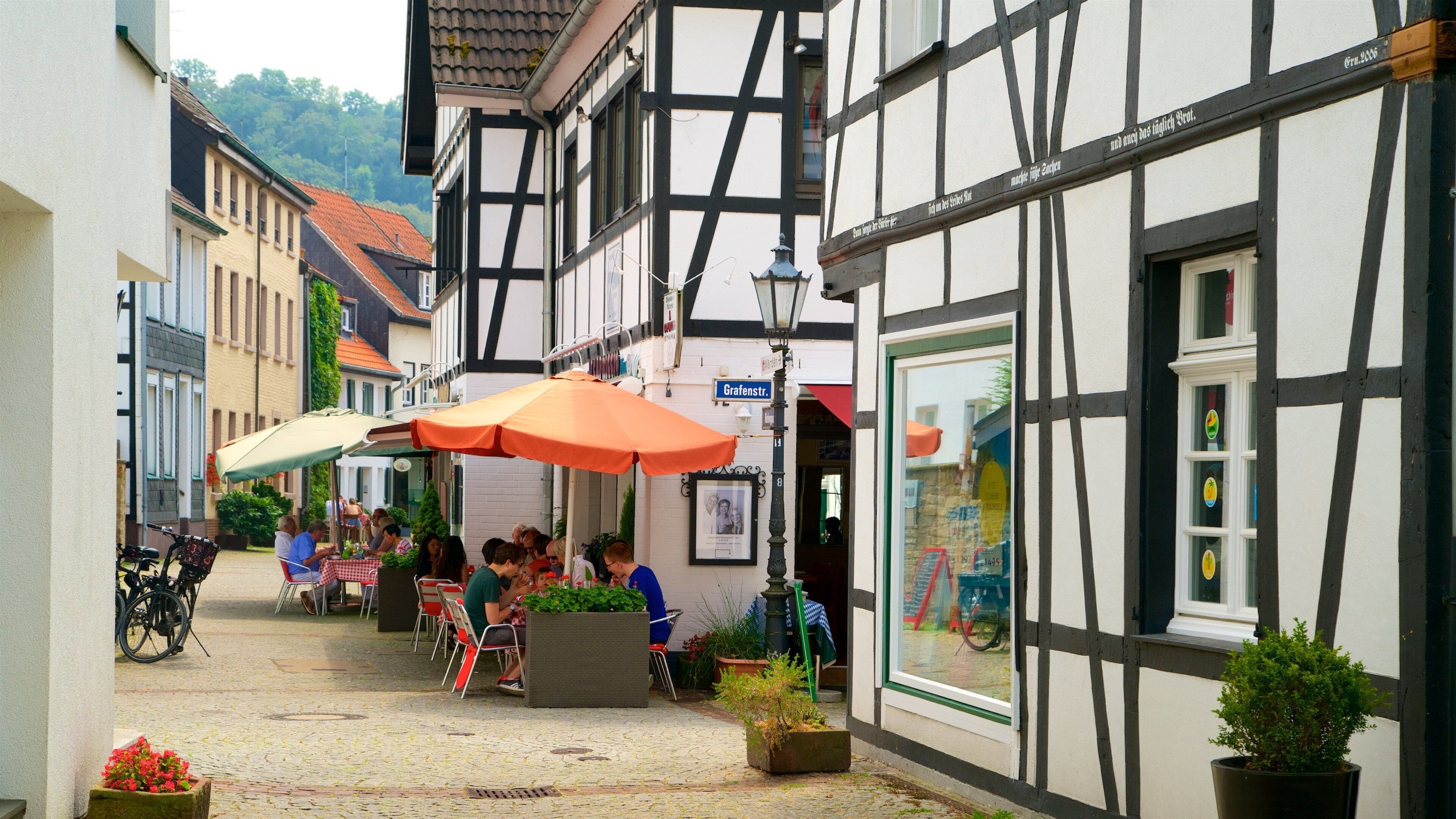 A cobblestone street with half-timbered buildings, outdoor seating, and bicycles.