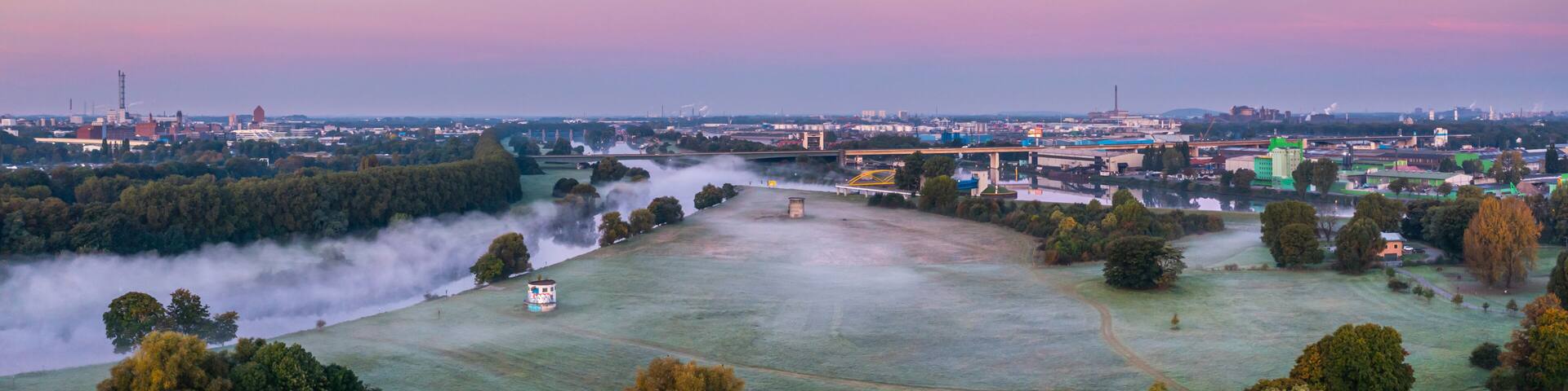 A cityscape with a river, industrial buildings, and a bridge.