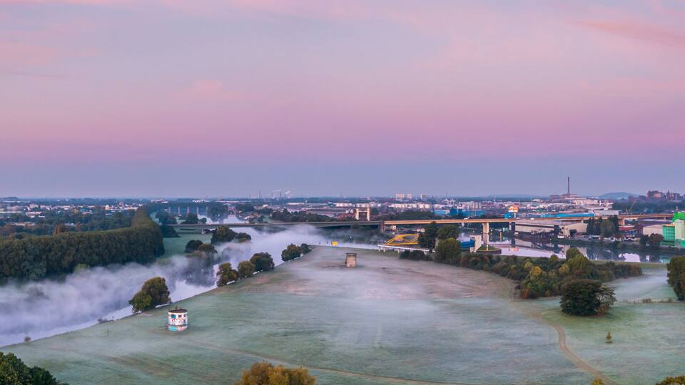 A cityscape with a river, industrial buildings, and a bridge.