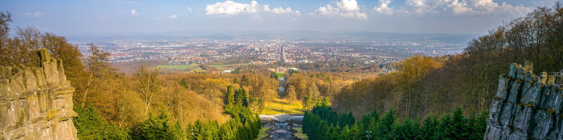 A stone pathway leading through a forested area with a city in the background.