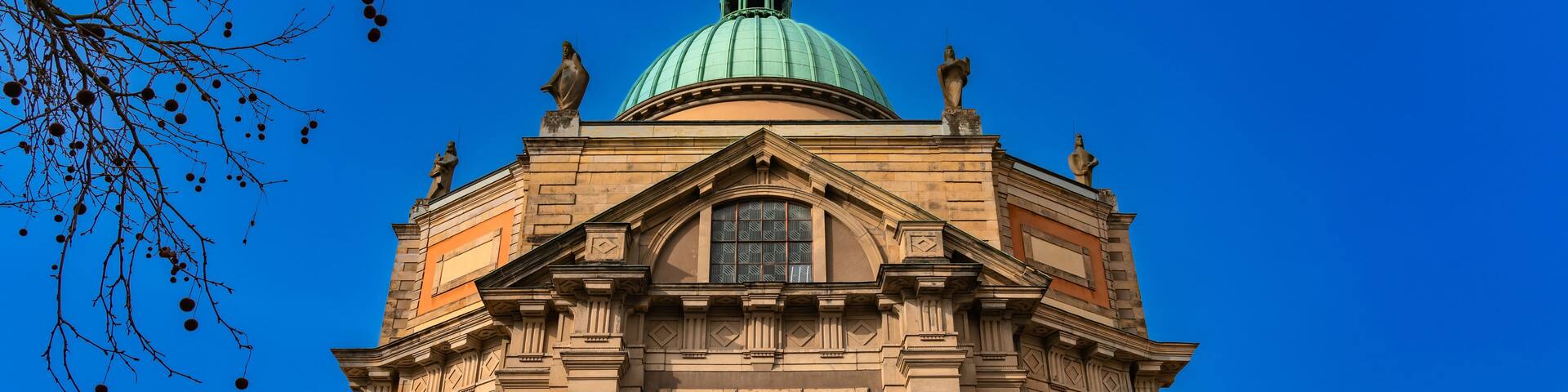 A historic building with a green dome, ornate facade, and statues.