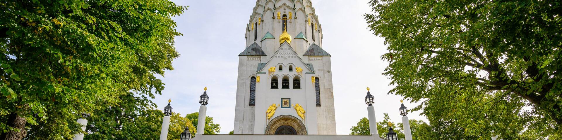 A church with a tall spire, surrounded by trees and a flower bed.
