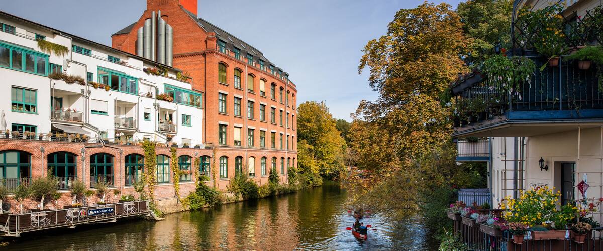 Ein Kanal mit Gebäuden an beiden Seiten, ein Boot mit Personen und Herbstlaub.