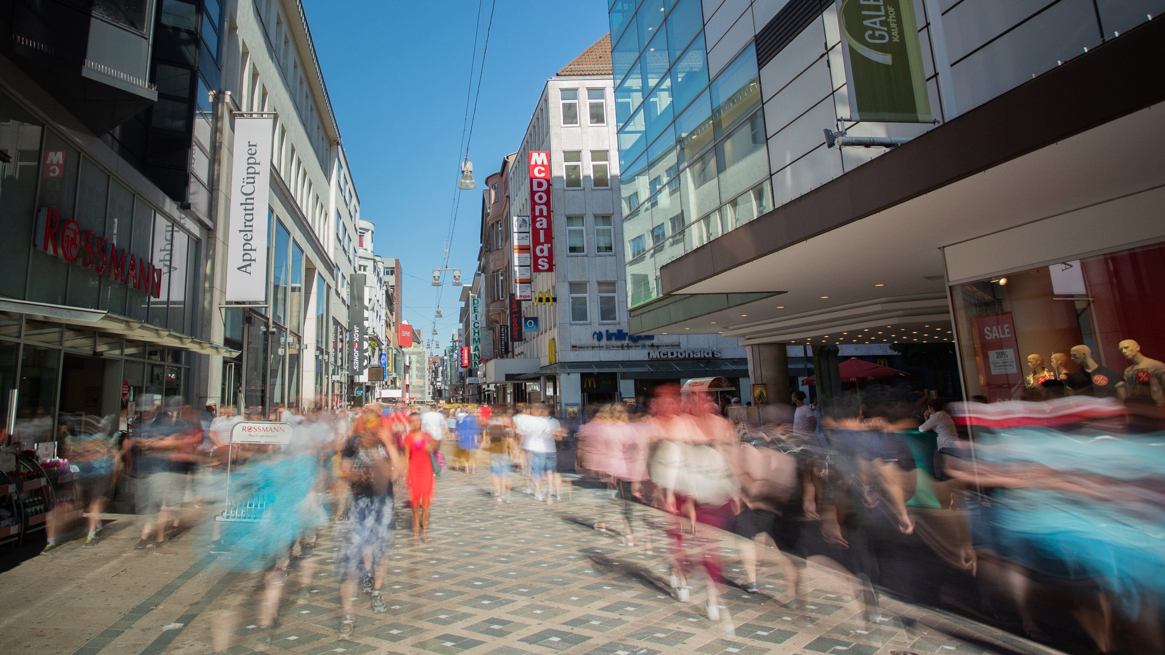 A busy urban street with various storefronts, including a McDonald's and a Rossmann store.
