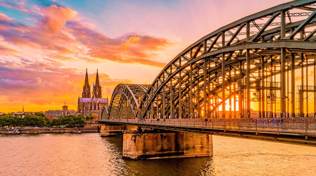 A steel bridge over a river with a cathedral in the background during sunset.