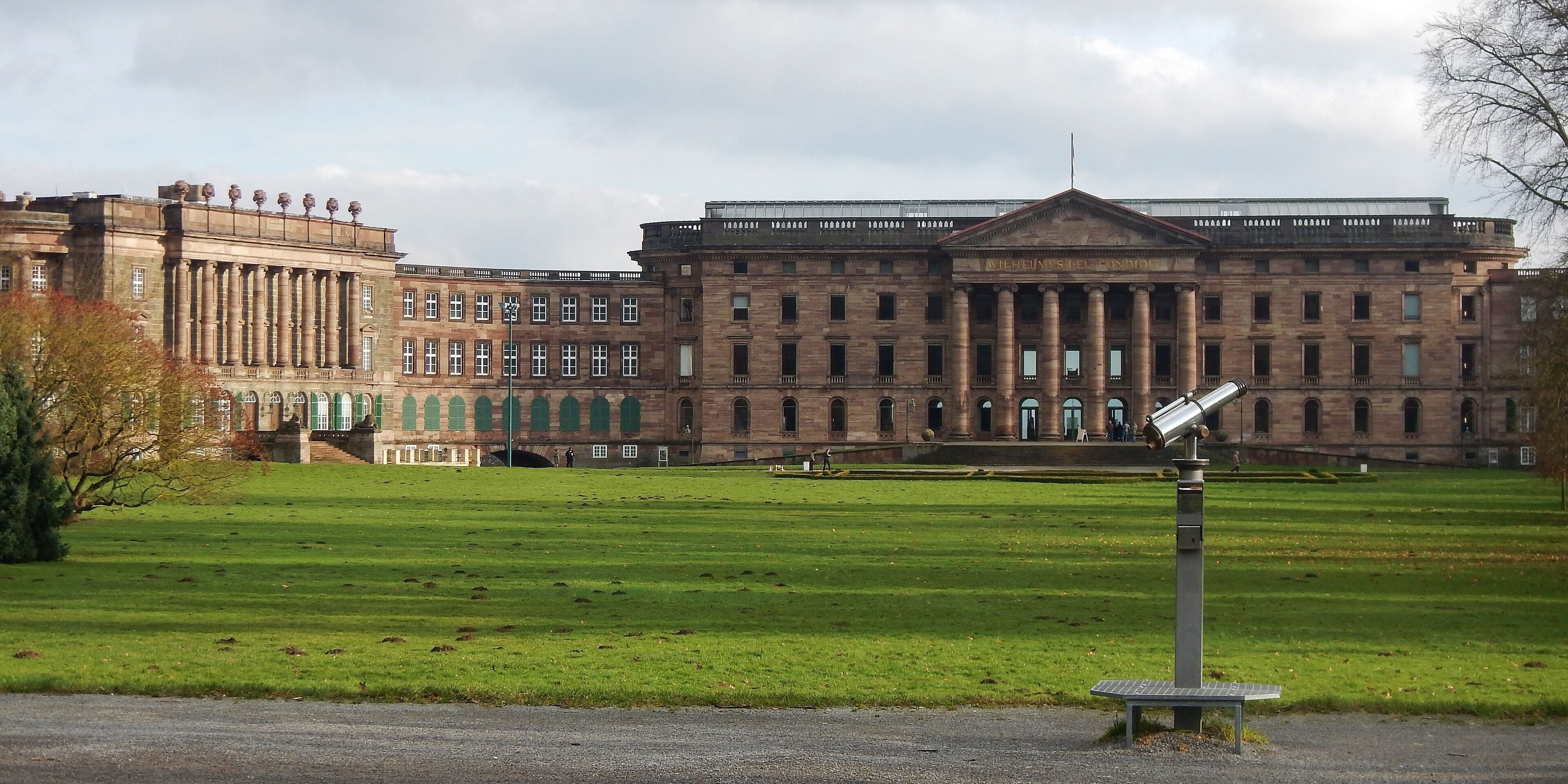A large historic building with columns and a central entrance, surrounded by a well-maintained lawn.