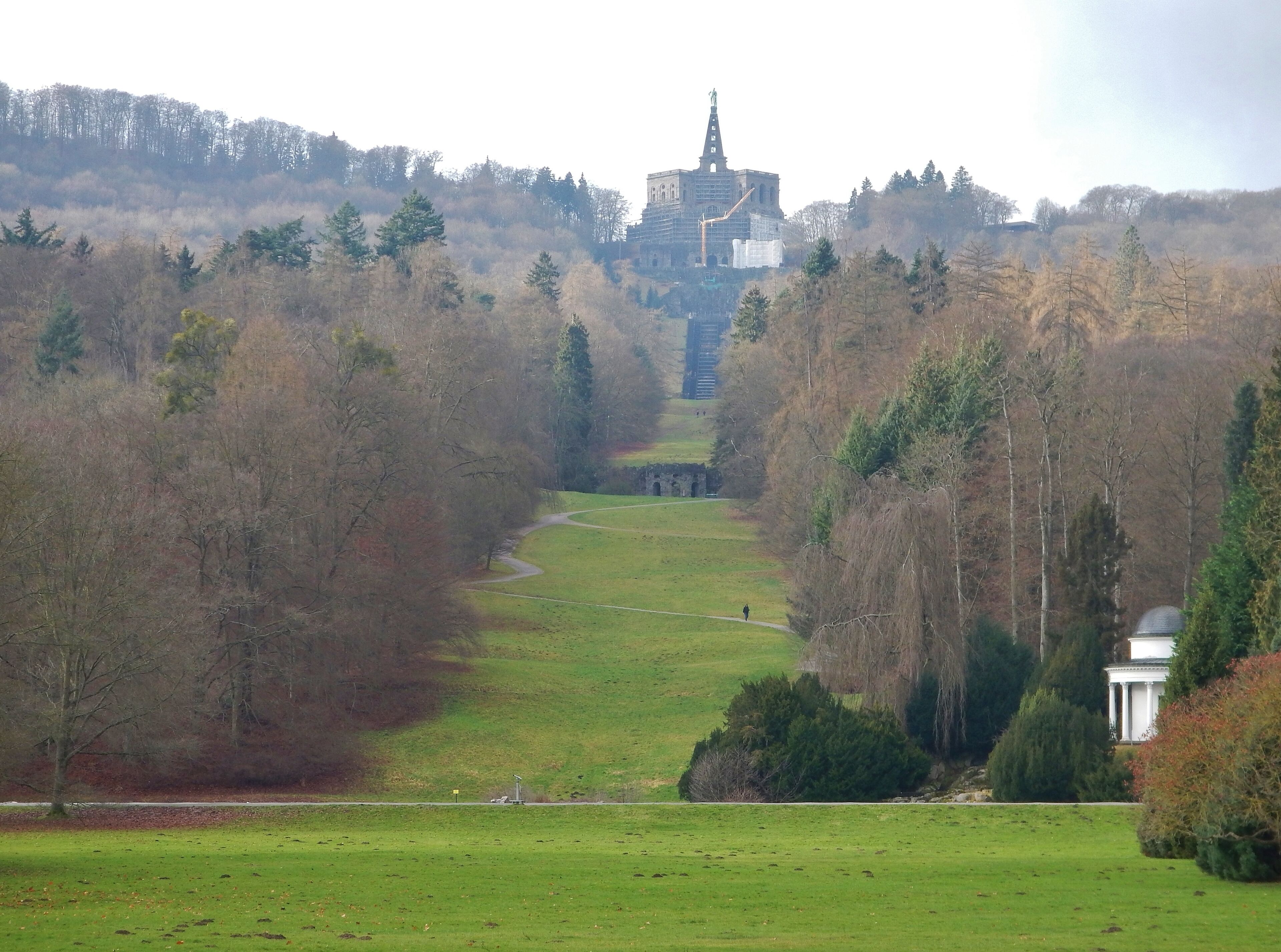 A park with a large open field, a pathway, and a historic building with a tower.