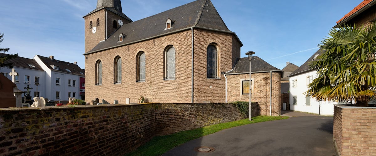 Historic European red brick church (St. Jakobus) with a slate steeple and clock tower, seen from a narrow street in Cologne Widdersdorf, Germany