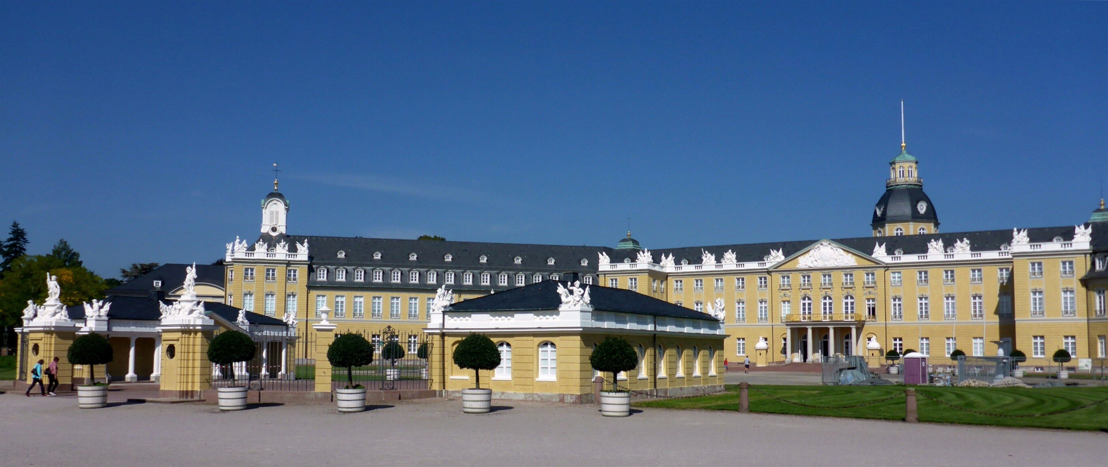 A large yellow building with a green dome and statues in front.