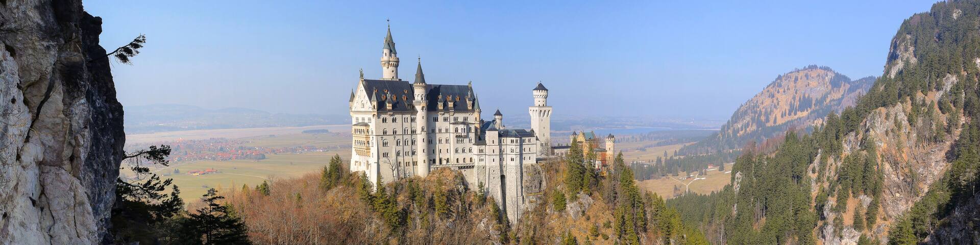 A castle on a hill with a forested mountain backdrop.