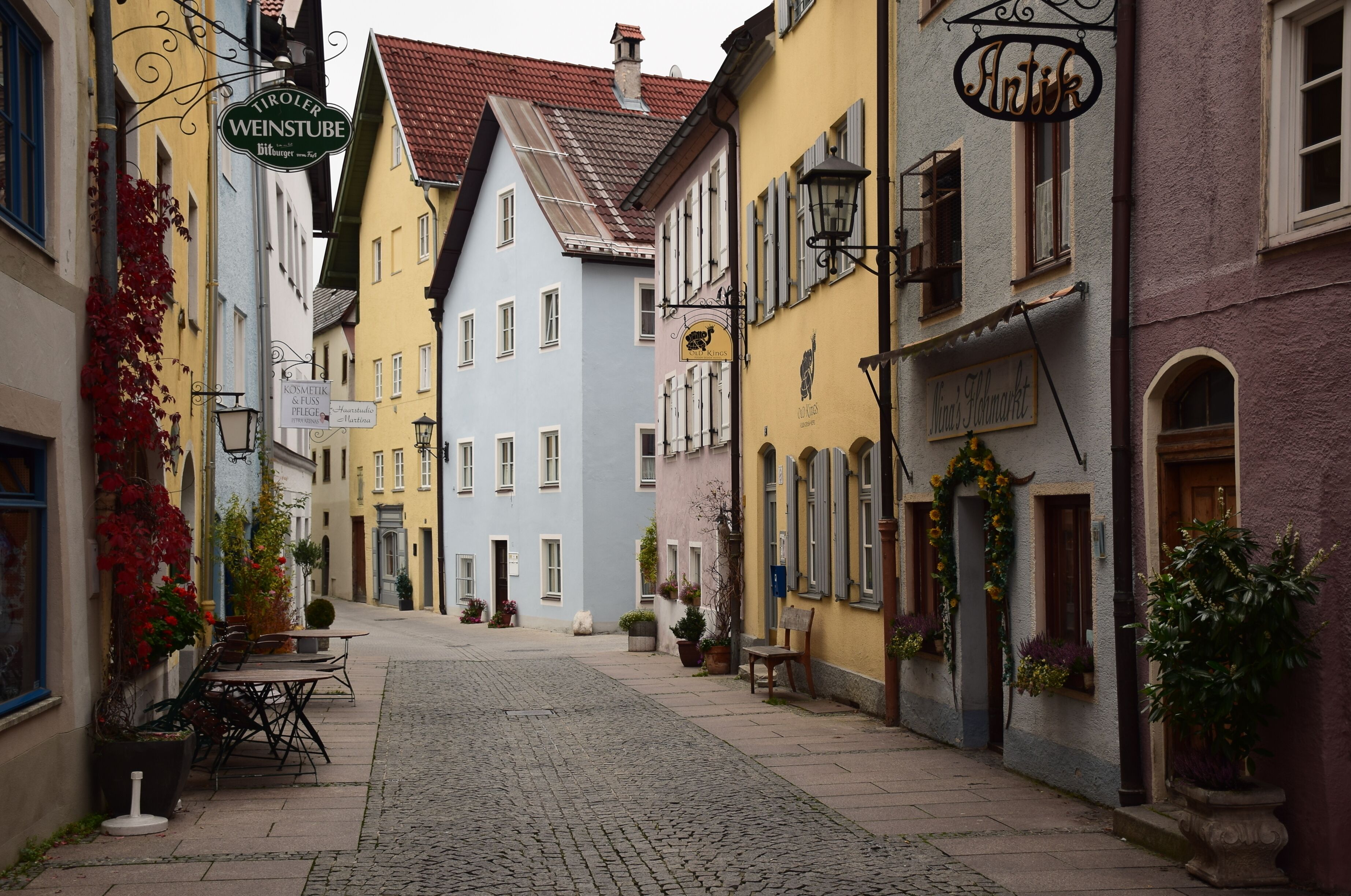 Uma rua de paralelepípedos ladeada por edifícios coloridos, incluindo uma placa com a inscrição "Tiroler Weinstube".