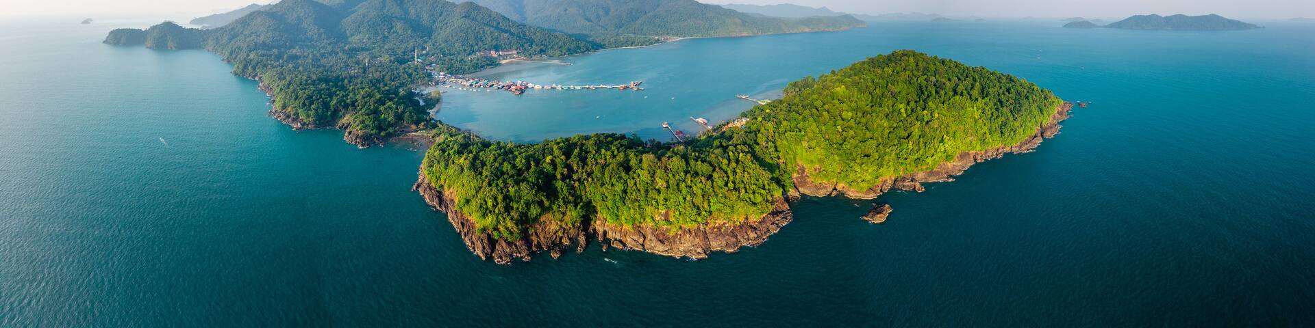 An aerial view of a lush green island surrounded by clear blue waters, with a small settlement and a pier.