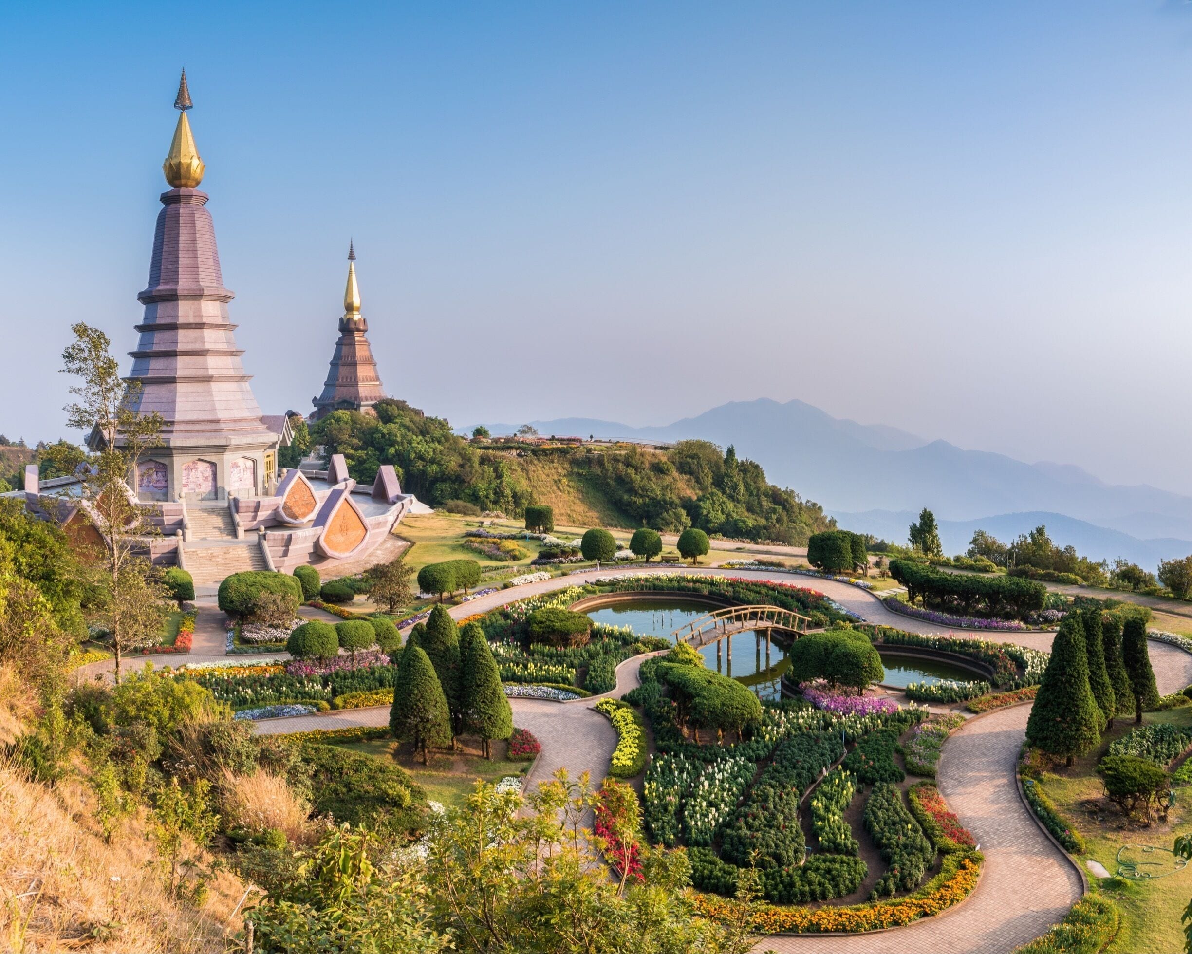 A pagoda with two golden spires, surrounded by a well-maintained garden with a pond and winding paths.
