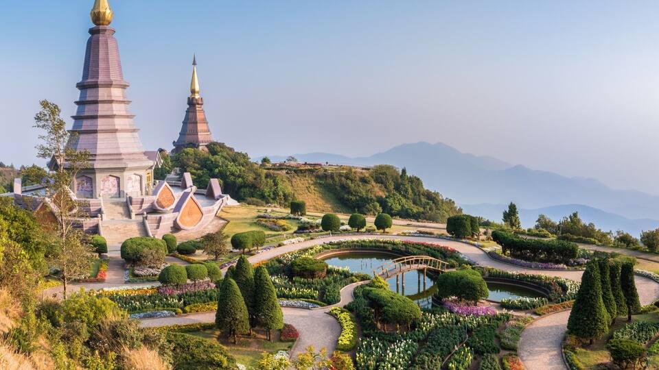 A pagoda with two golden spires, surrounded by a well-maintained garden with a pond and winding paths.