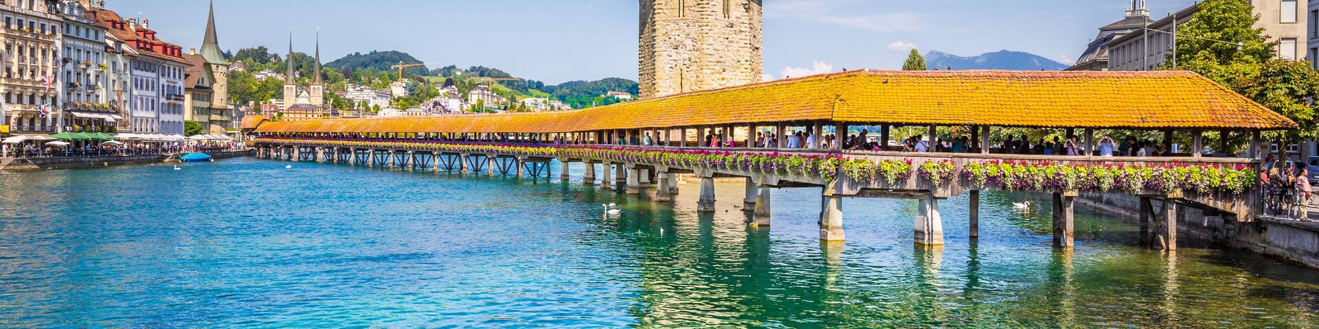 A historic tower with a conical roof, a bridge with yellow awnings, and a calm river reflecting the sky.