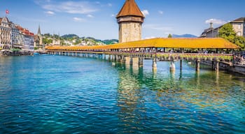 A historic tower with a conical roof, a bridge with yellow awnings, and a calm river reflecting the sky.