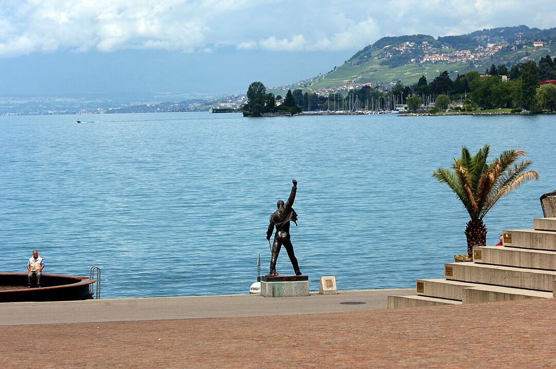 Una estatua junto a la costa, una palmera y un pueblo distante al otro lado del agua.