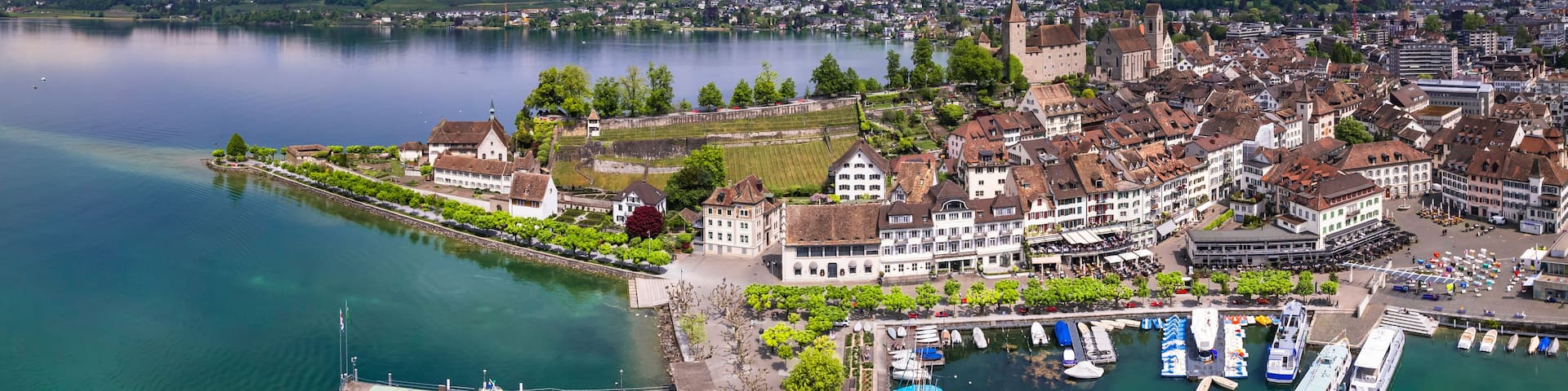 A lakeside town with historic buildings, a boat dock, and a castle in the background.
