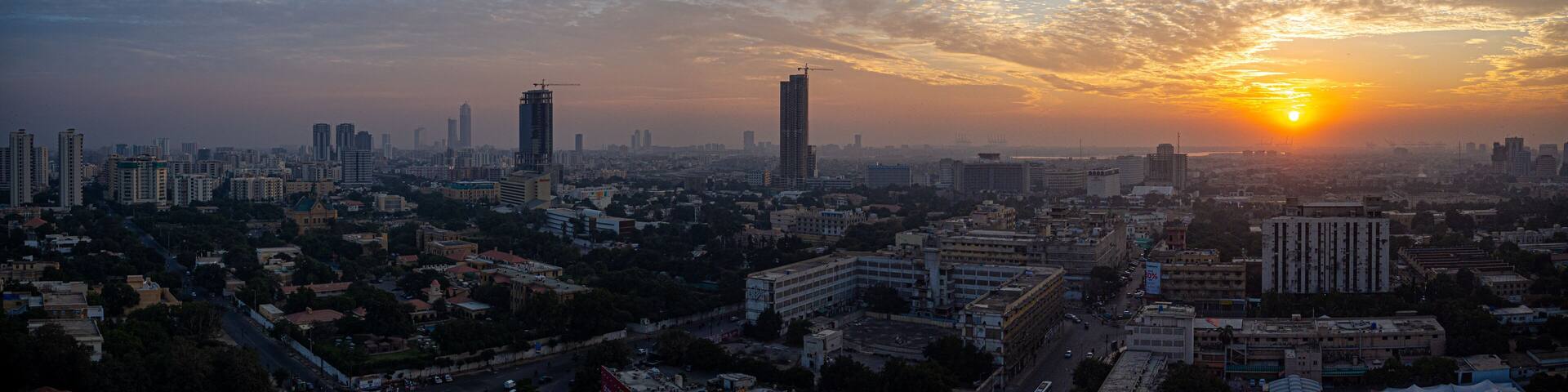 A cityscape at sunset with a prominent skyscraper and a construction crane.