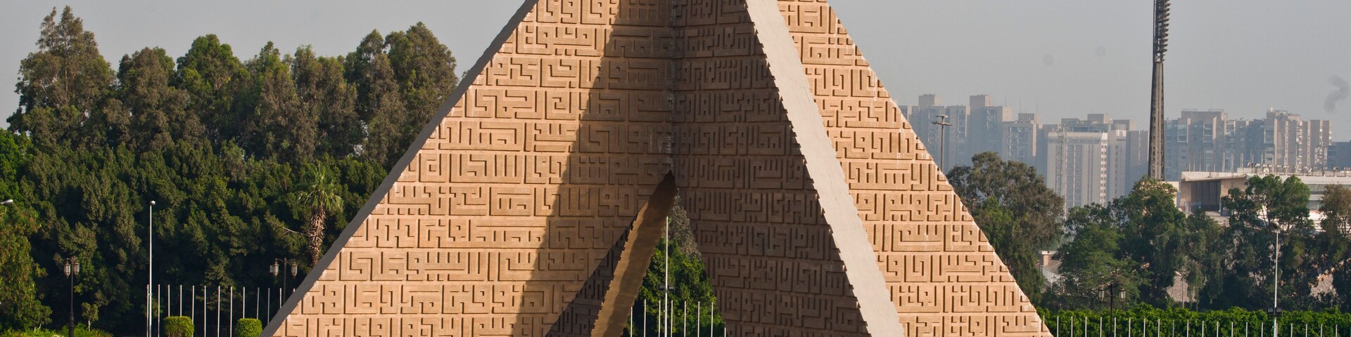 Ein großes, dreieckiges Denkmal mit aufwendigen Mustern, umgeben von einem Spiegelteich und Bäumen.