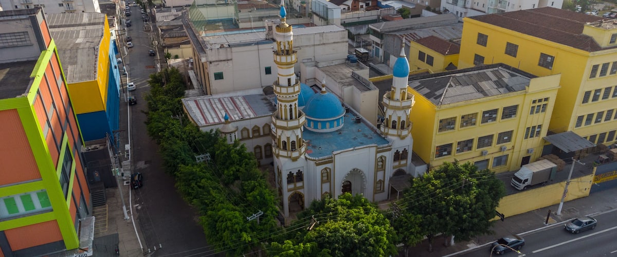 Städtische Landschaft mit einer markanten Moschee, die blaue Kuppeln und einen Minarett aufweist, umgeben von farbenfrohen Gebäuden und einer belebten Straße.