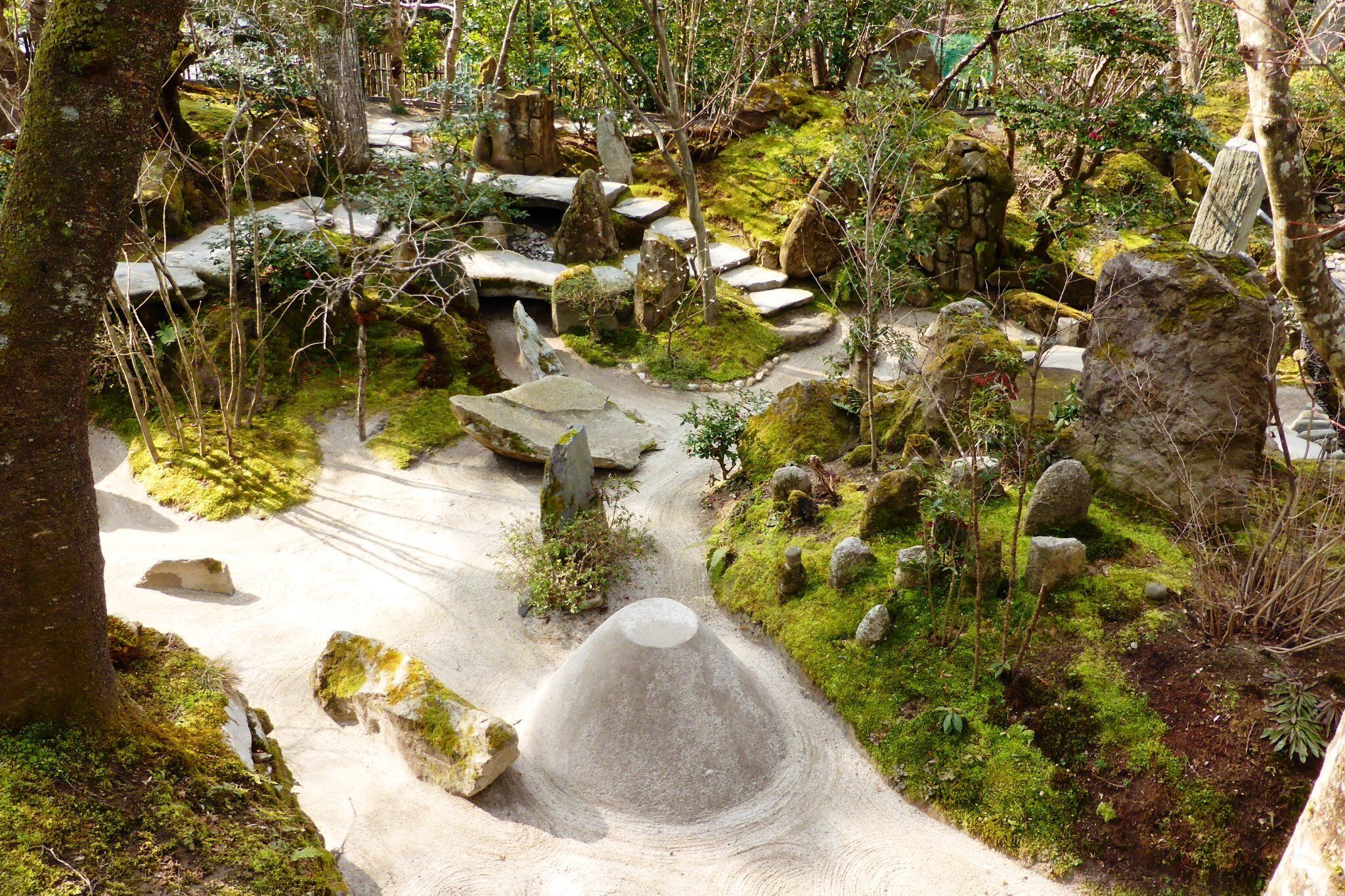 A forested area with a stone pathway, moss-covered rocks, and a small pond.
