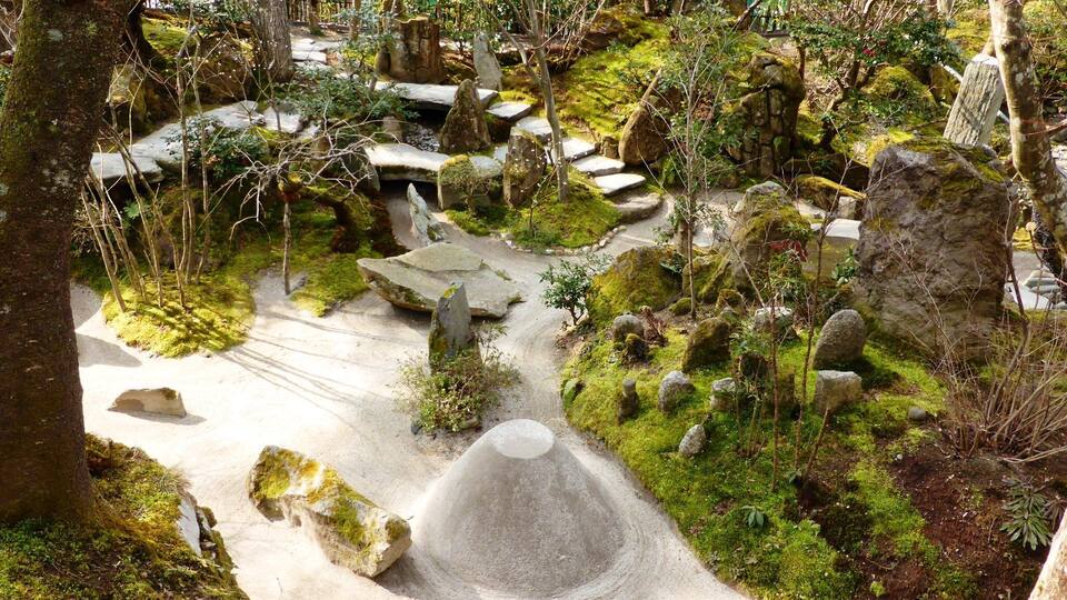 A forested area with a stone pathway, moss-covered rocks, and a small pond.