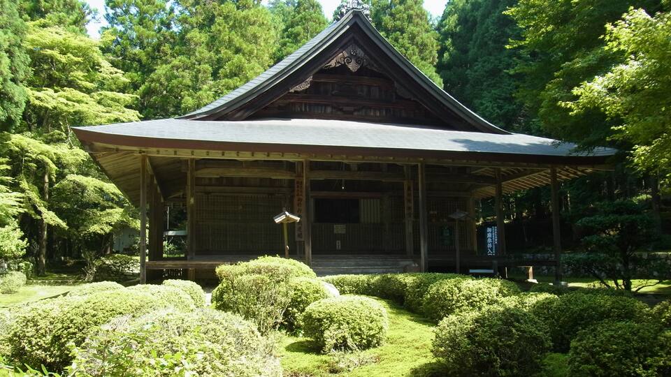 A traditional Japanese building surrounded by lush greenery and a small stream.
