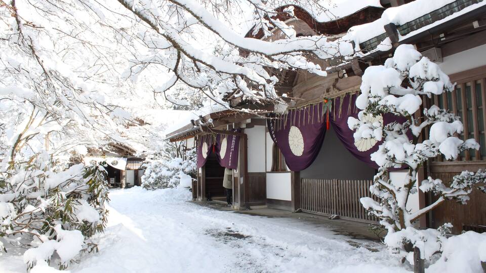 A traditional Japanese building with snow-covered trees and a wooden fence.