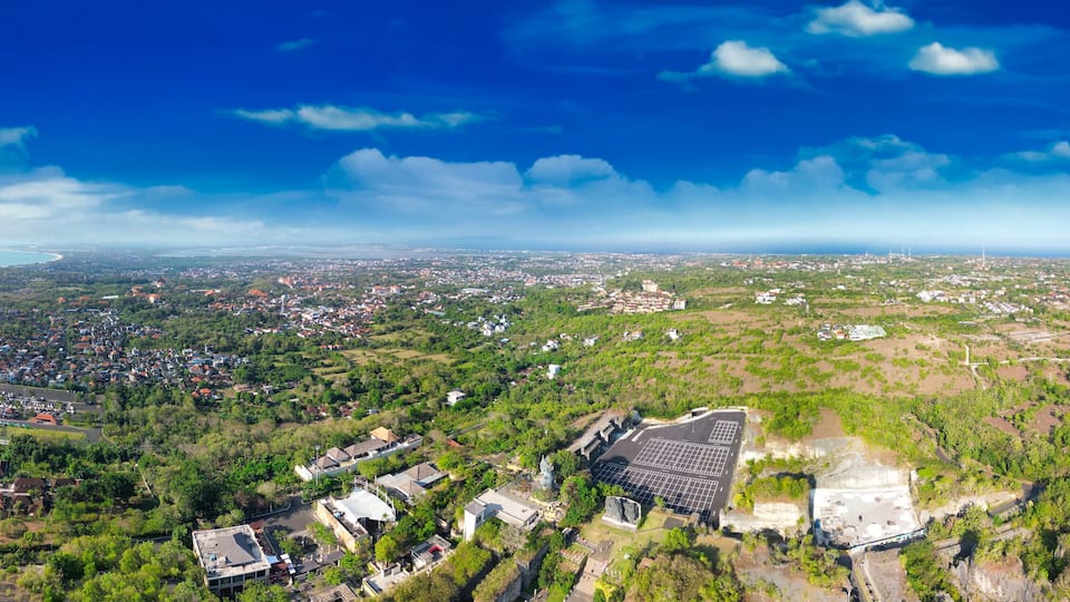 Une vue aérienne d’une ville avec une grande statue, des collines verdoyantes et une côte.
