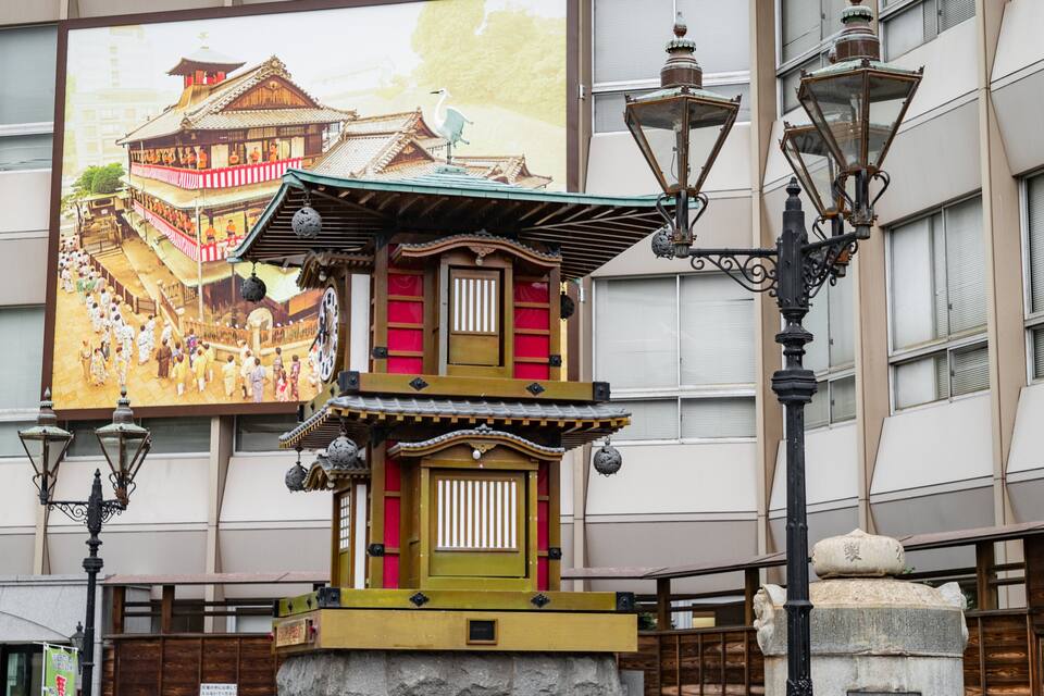 A traditional Japanese building with a pagoda-style roof, a stone lantern, and a large mural of a temple in the background.