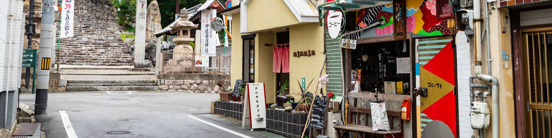 A narrow street with traditional Japanese architecture, including a shrine and a colorful storefront.
