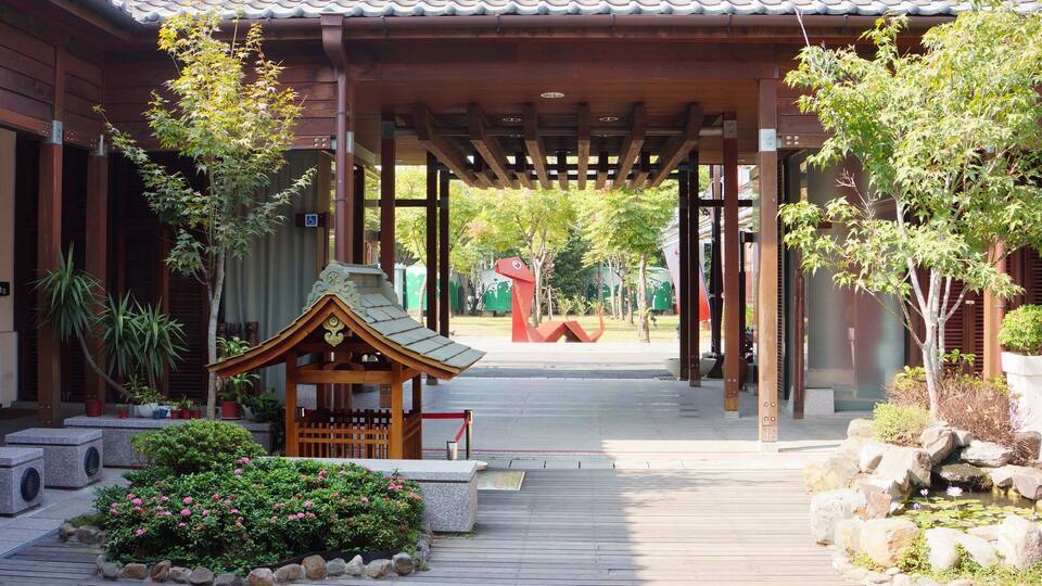 Ein traditionelles japanisches Gebäude mit einem Ziegeldach, einem hölzernen Gang und einem kleinen Garten mit Steinen und Blumen.