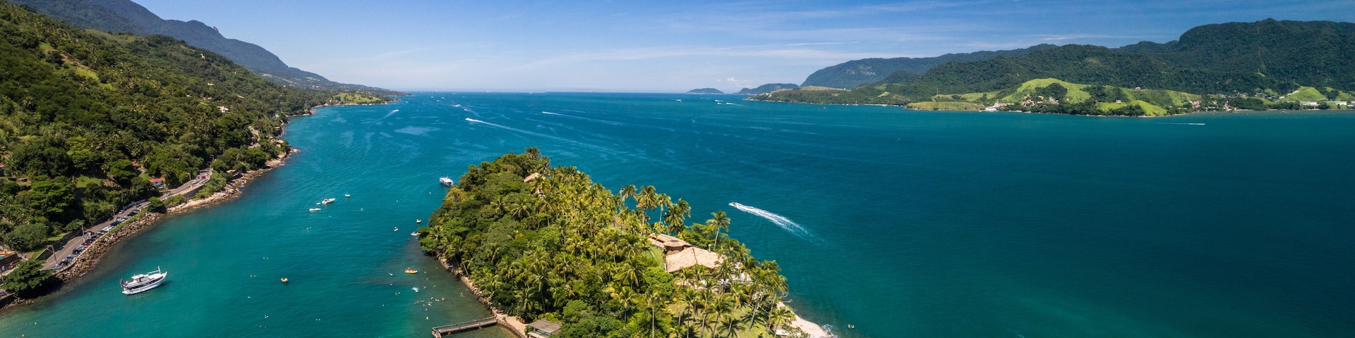 Une île tropicale entourée d’eaux turquoise, avec des bateaux et un ciel dégagé.
